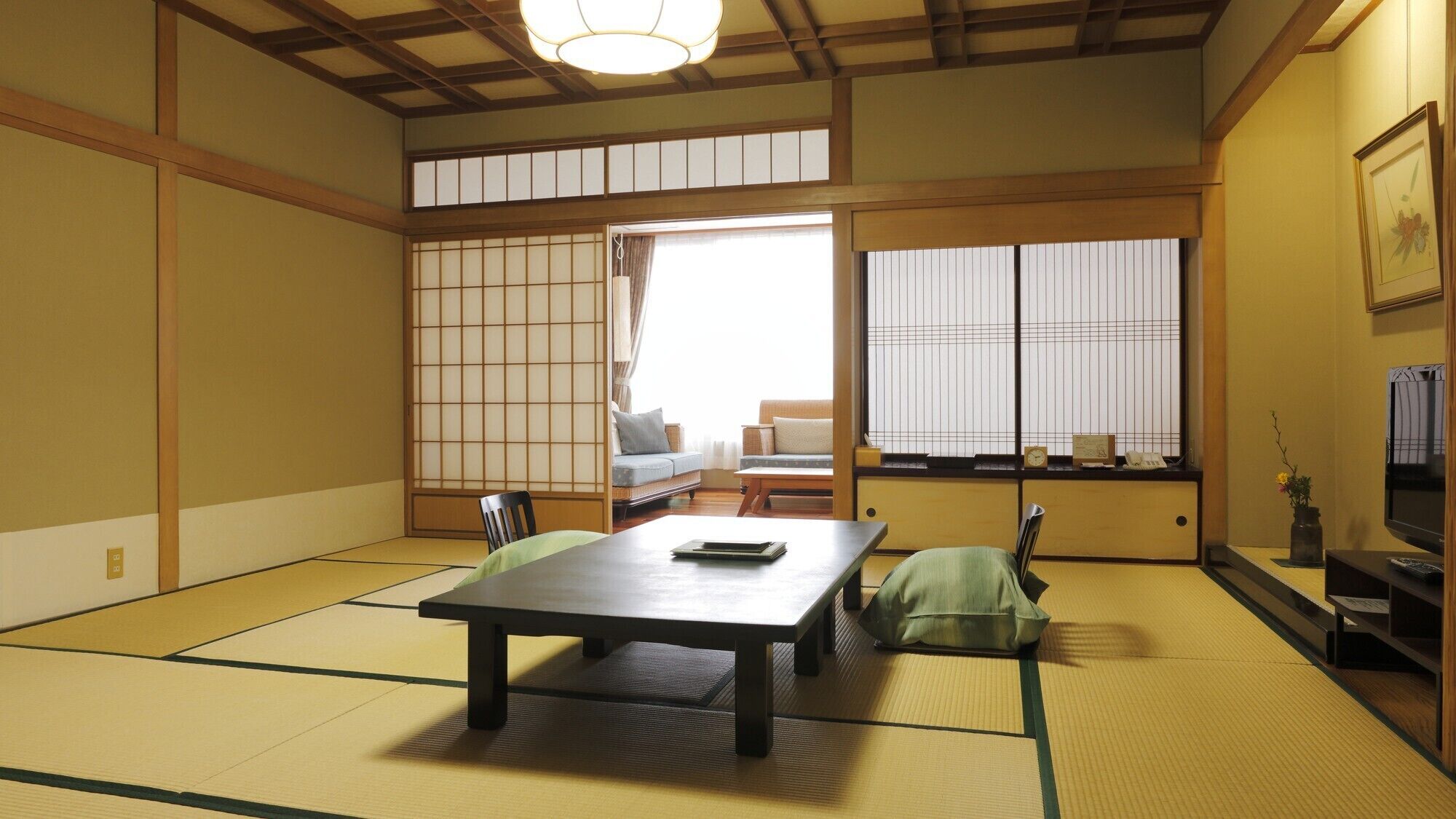 Una habitación japonesa tradicional con suelo de tatami, una mesa baja, un sofá, puertas correderas shoji y un televisor.