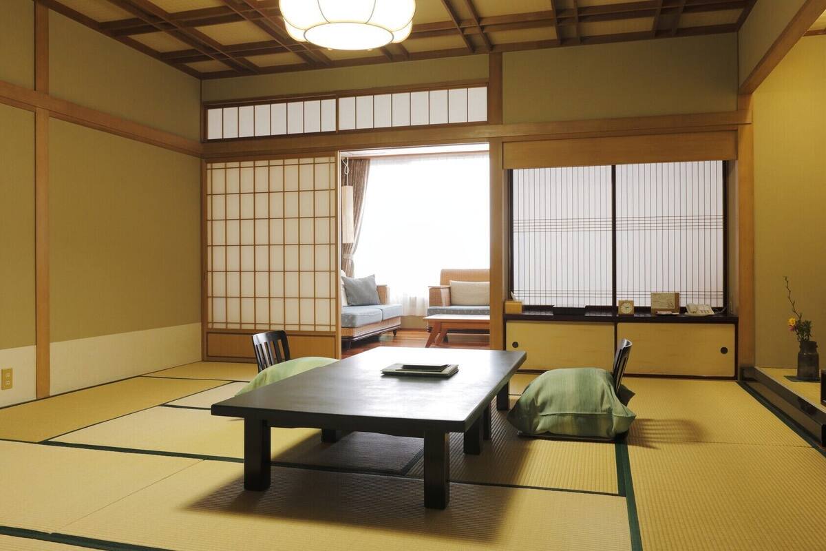 Una habitación japonesa tradicional con suelo de tatami, una mesa baja, un sofá, puertas correderas shoji y un televisor.