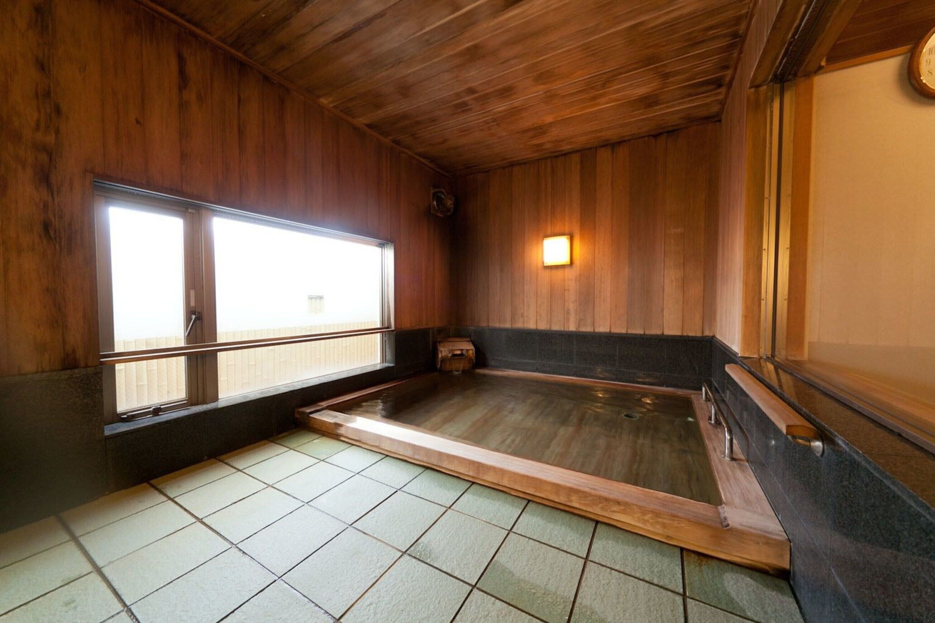 Ett traditionellt japanskt onsen med väggar och badkar av trä samt ett golv täckt med kakel.