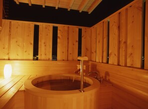 A wooden sauna with a circular hot tub, wooden walls, and a bench.