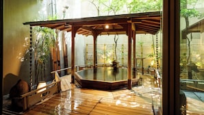 A traditional Japanese onsen with a wooden deck, a stone bath, and bamboo plants. - Hatori (Kaga)
