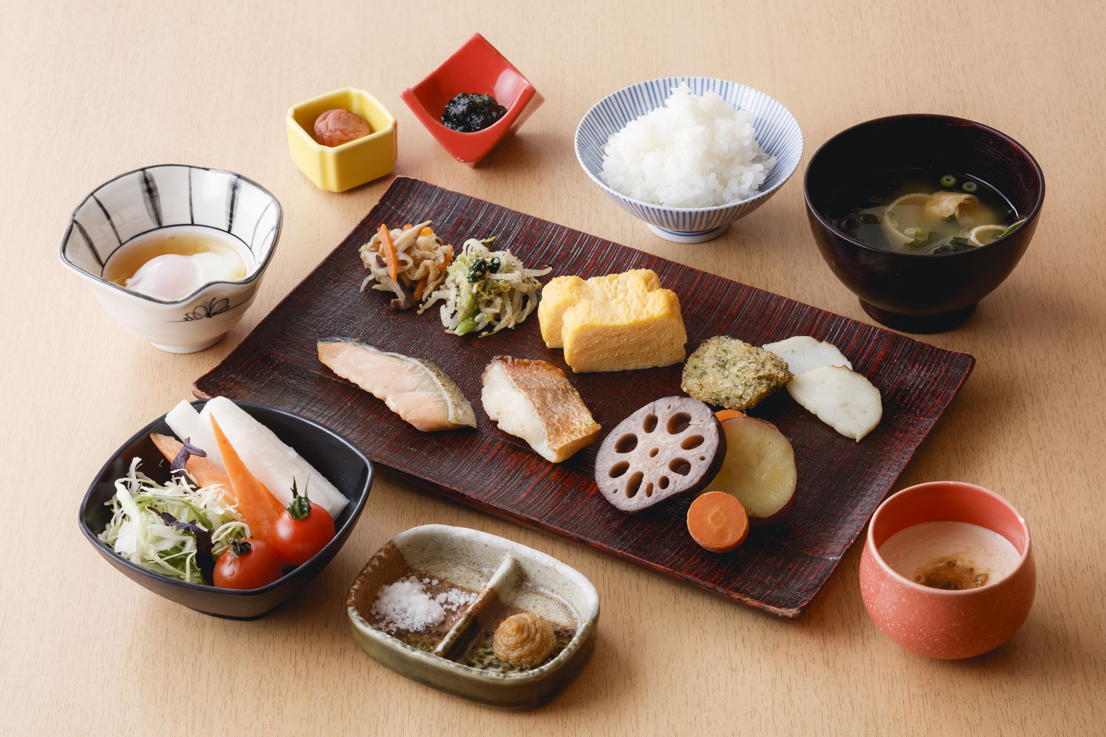 A variety of Japanese dishes including sushi, tempura, and a bowl of soup, arranged on a wooden table.