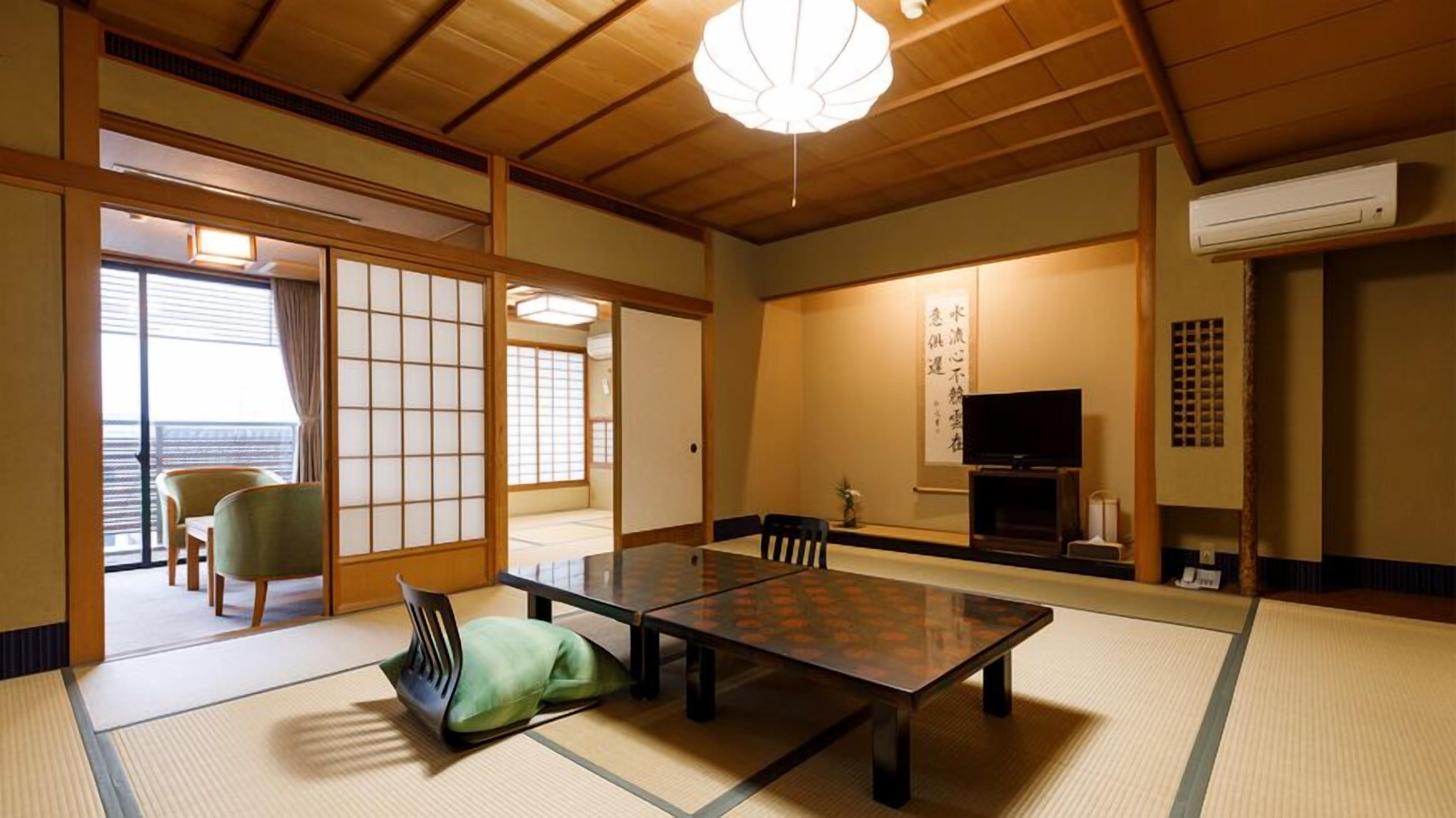 Una habitación japonesa tradicional con suelo de tatami, una mesa baja, sillas, un televisor y una puerta corredera.