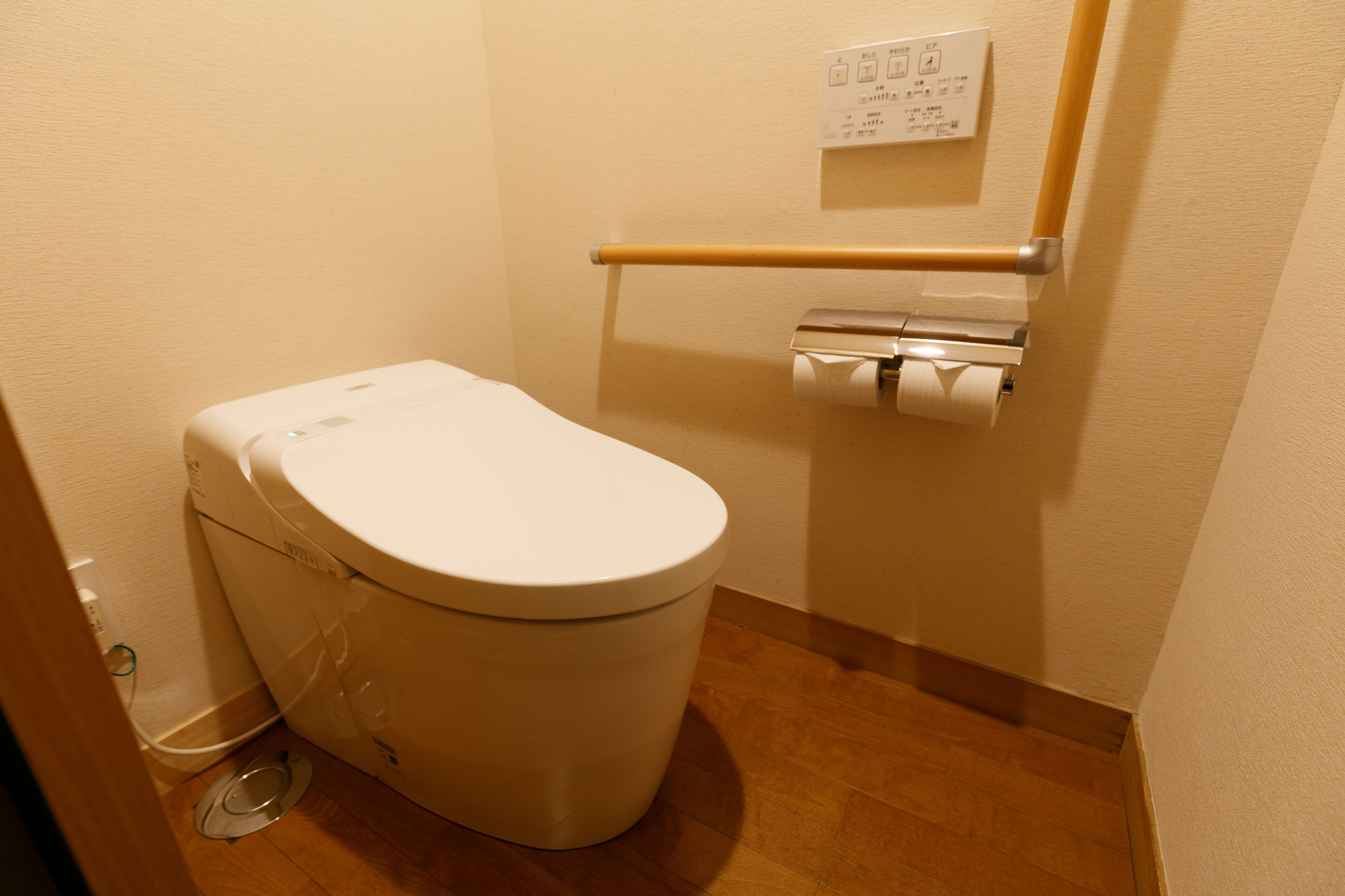 A small, clean bathroom with a white toilet, a toilet paper holder, and a flush handle.