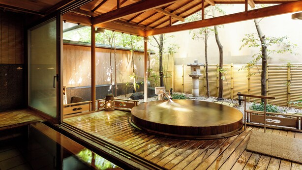 A traditional Japanese onsen with a wooden deck, a hot spring bath, and a view of bamboo and trees. - Hatori (Kaga)