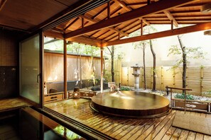 Un onsen japonés tradicional con terraza de madera, baño de aguas termales y vistas a bambú y árboles.