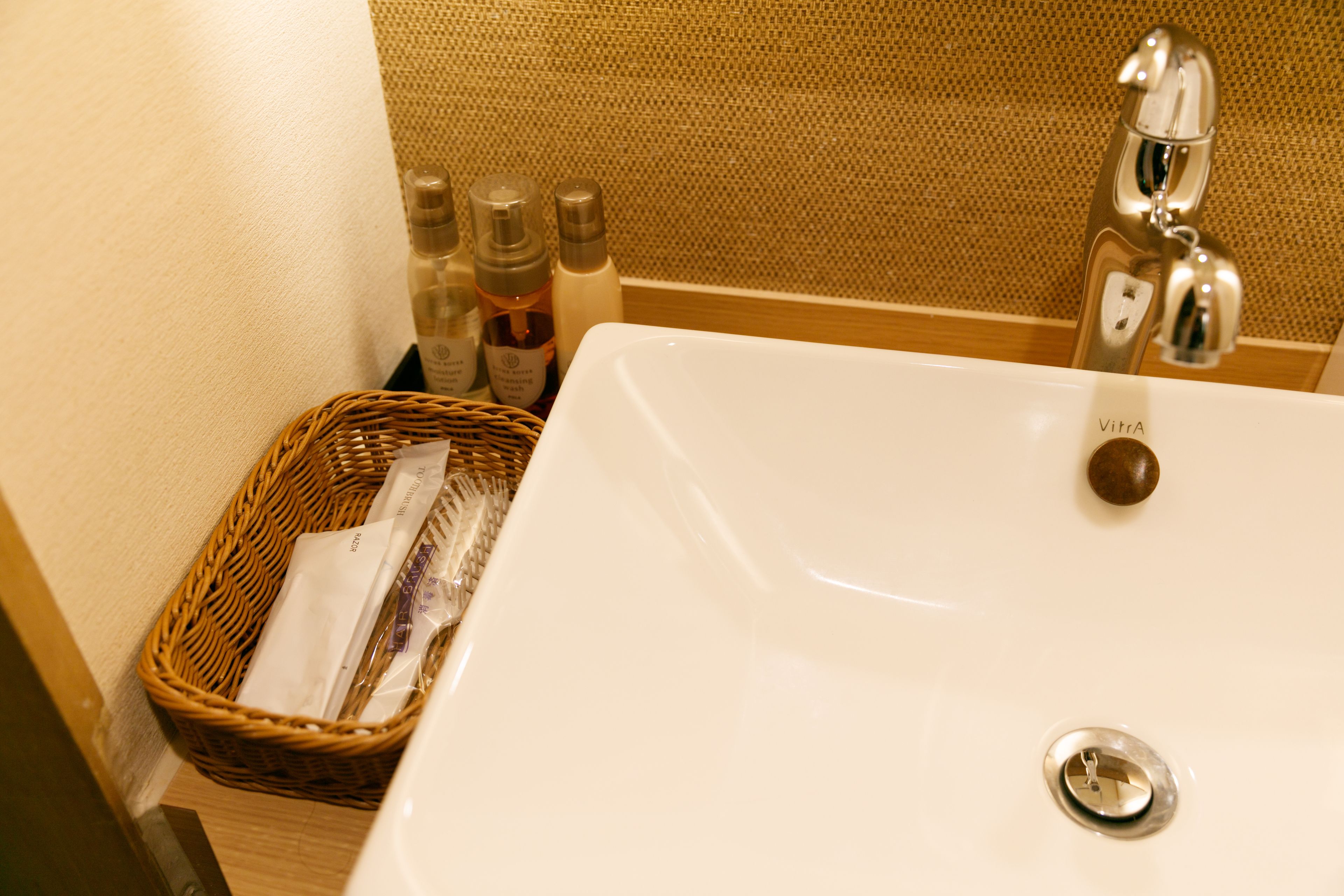 A bathroom sink with a chrome faucet, a wicker basket with toiletries, and a textured wall in the background.