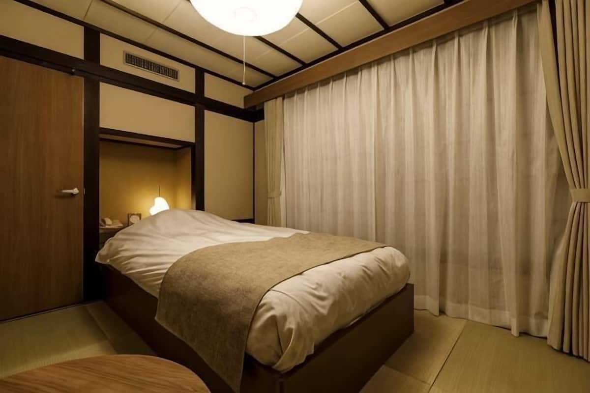 Una habitación con cama, mesita de noche, lámpara y ventana con cortinas.