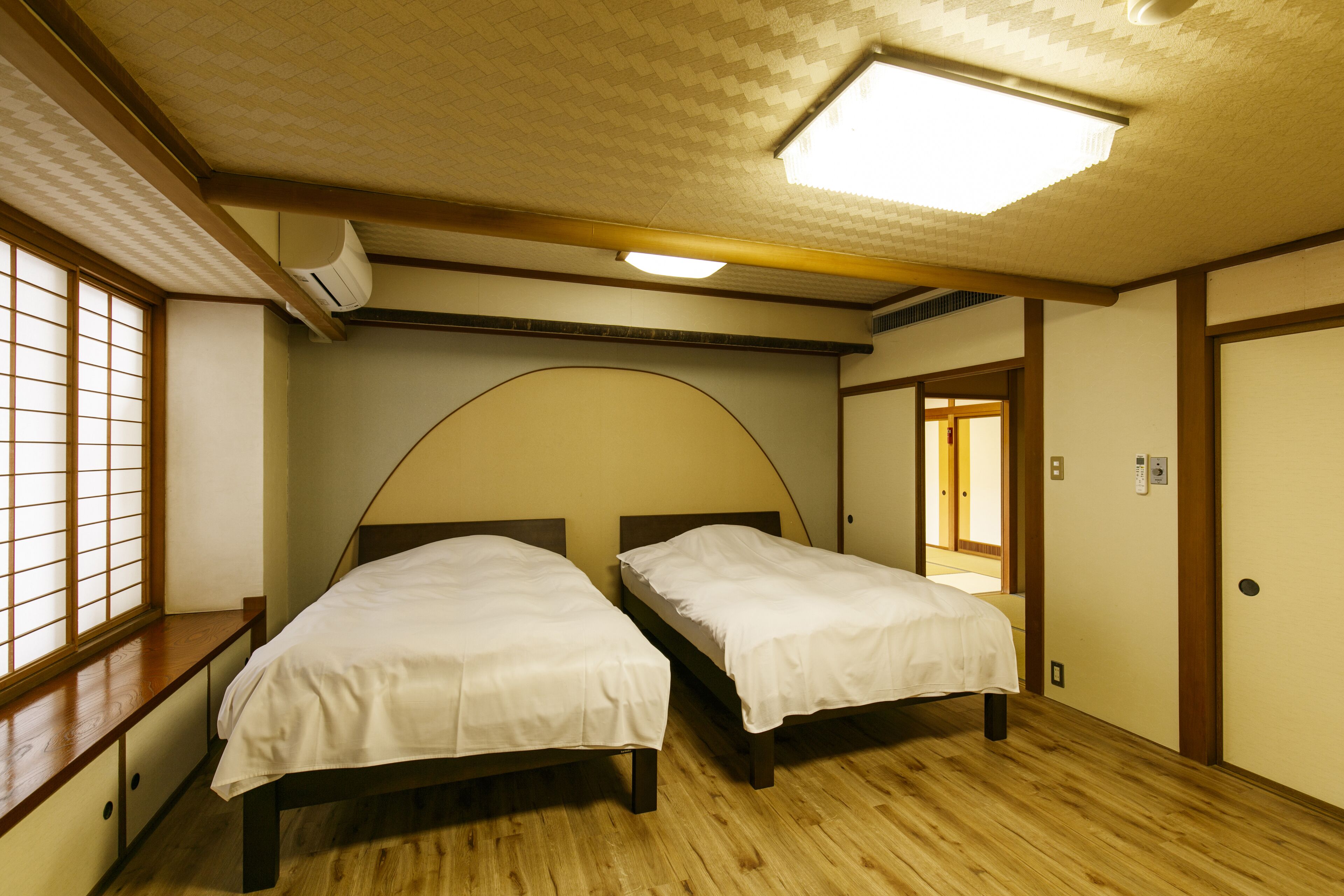 Una habitación con dos camas, suelo de madera, un ventanal con vistas y un ventilador de techo.