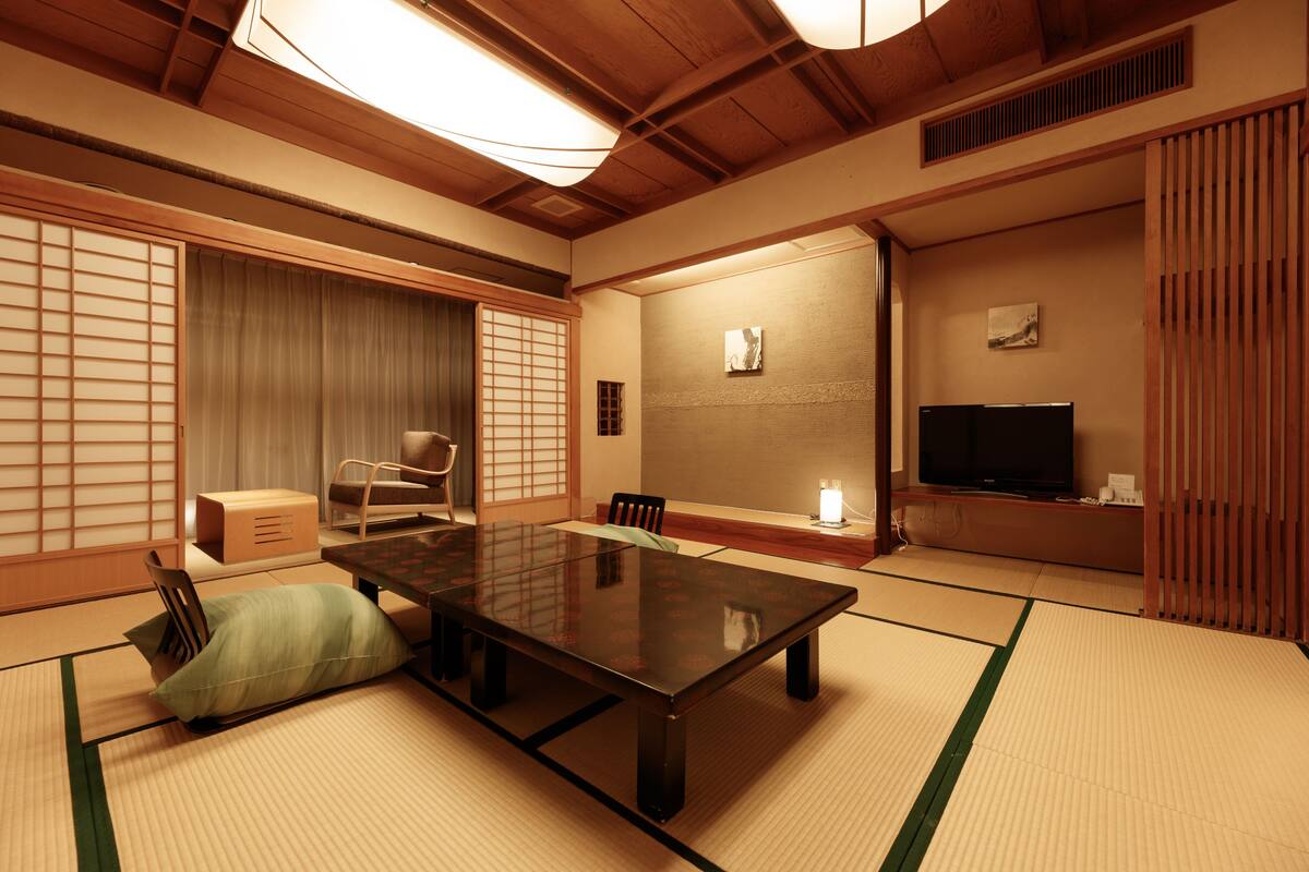 Una habitación japonesa tradicional con suelo de tatami, una mesa baja, un televisor y puertas correderas.