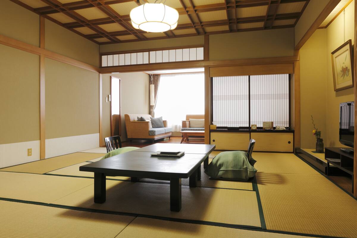 Una habitación japonesa tradicional con suelo de tatami, una mesa baja, un sofá y puertas correderas que dan a otra estancia.