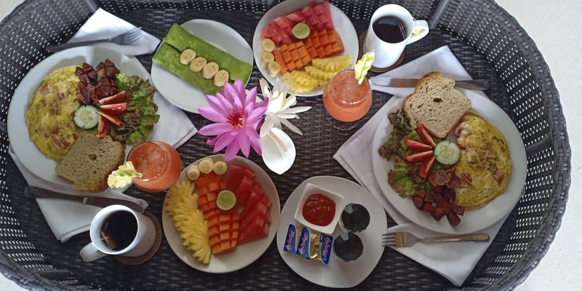 Bandeja de desayuno con diversos platos, como huevos, tostadas y fruta, junto con salsas y un centro de mesa floral.
