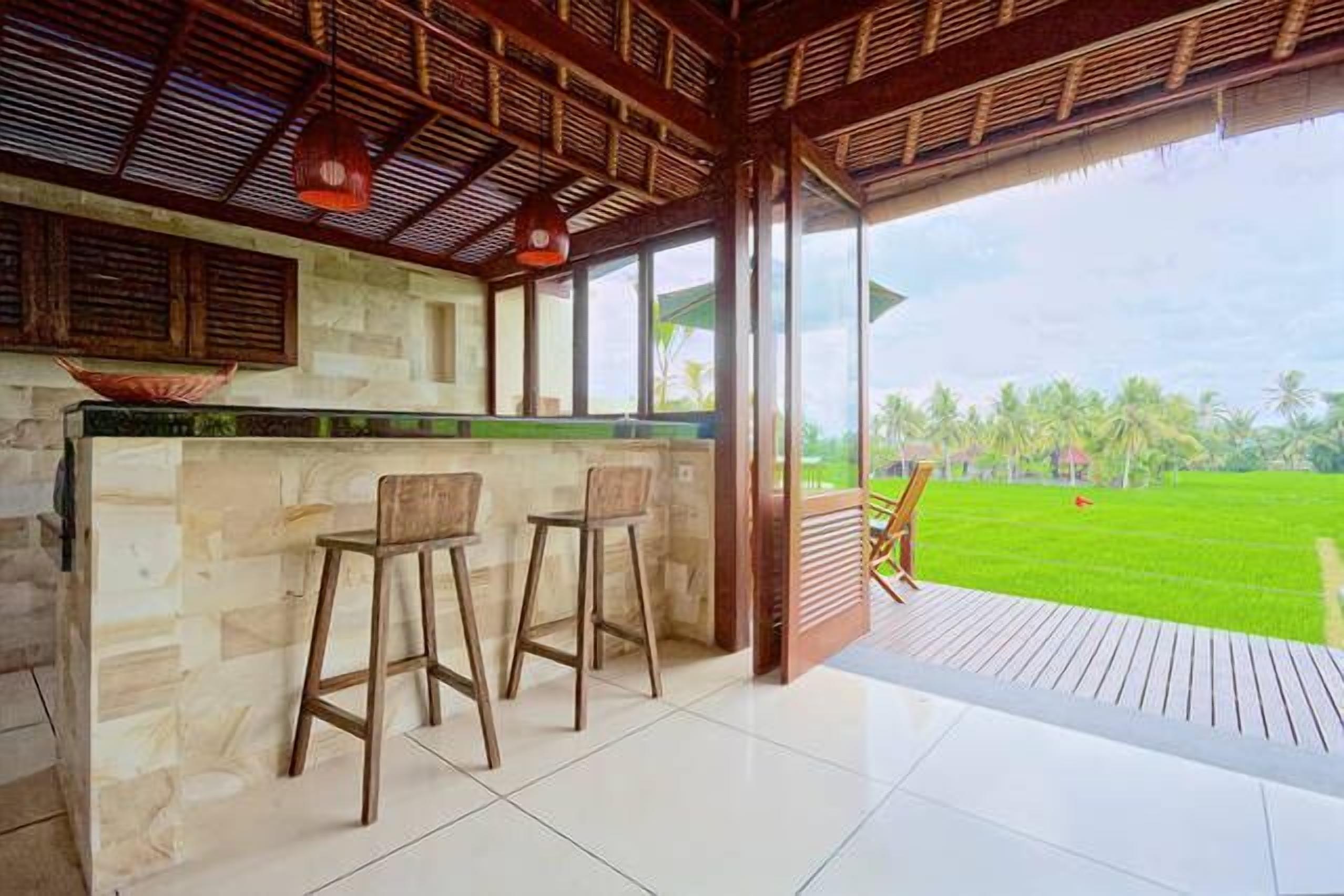 A bar area with a stone counter and two wooden stools, overlooking a lush green landscape.