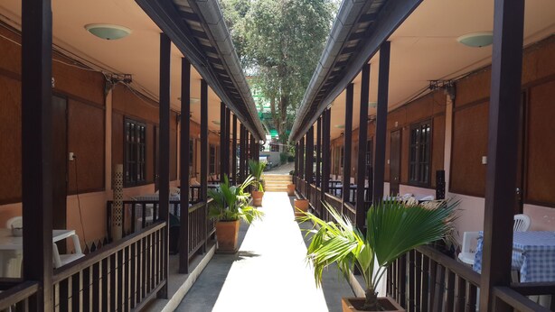 A covered corridor with wooden pillars, potted plants, and tables with checkered tablecloths. - Lucky Home Resort (Koh Samui)