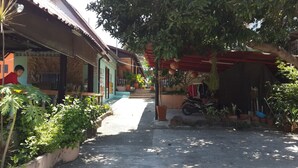 A narrow street with buildings on either side, potted plants, and a motorcycle parked on the right. - Lucky Home Resort (Koh Samui)
