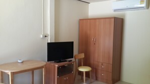 A small room with a wooden cabinet, a television on a stand, a small table, and a chair. - Lucky Home Resort (Koh Samui)
