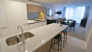 A modern kitchen with a large island, a dining area with a TV, and a view of the city through large windows. - Chester Hotel (Fortitude Valley)
