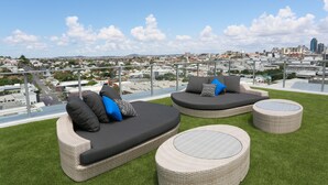 A rooftop terrace with two curved sofas and two round tables, offering a view of a cityscape. - Chester Hotel (Fortitude Valley)