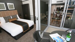 A hotel room with a bed, a dining table with a chair, a bottle, and a menu. - Chester Hotel (Fortitude Valley)