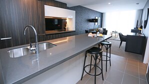 A modern kitchen with a large island, bar stools, and a dining area with a table and chairs. - Chester Hotel (Fortitude Valley)