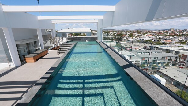 A modern rooftop pool with clear blue water, surrounded by white architecture and offering a view of the cityscape. - Chester Hotel (Fortitude Valley)