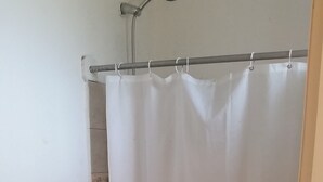 Une petite salle de bain avec des toilettes, une étagère en verre et un rideau de douche.
