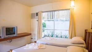 Une chambre d’hôtel avec deux lits, un téléviseur posé sur une étagère et une fenêtre avec des rideaux.