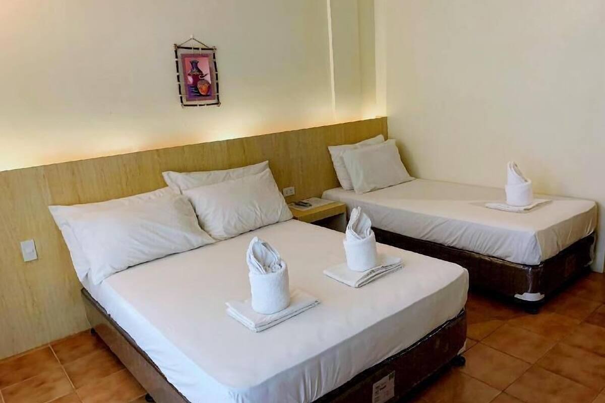 Une chambre d’hôtel avec deux lits, chacun agrémenté de draps et de serviettes blancs, d’une tête de lit en bois, d’une table de chevet et d’un petit tableau encadré accroché au mur.