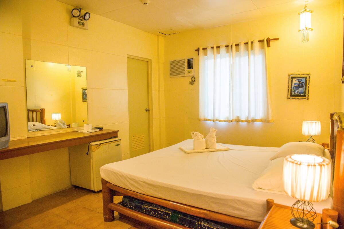 Une chambre d’hôtel comprenant un lit, une table de chevet, une lampe et un petit bureau avec un téléviseur.