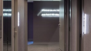 Un pasillo moderno con piso alfombrado, una lámpara empotrada en el techo y un letrero en la pared.