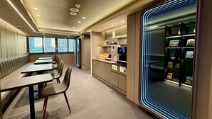 Un comedor moderno con mesas largas y sillas, una encimera de cocina con electrodomésticos y una vitrina con artículos.