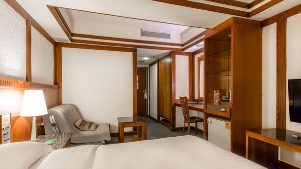 Una habitación de hotel con cama, escritorio, silla, televisor y minibar.
