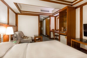 A hotel room with a bed, a desk, a chair, a television, and a minibar.