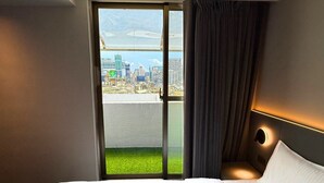 Una habitación de hotel con cama, un ventanal con vista a un paisaje urbano y una cortina.