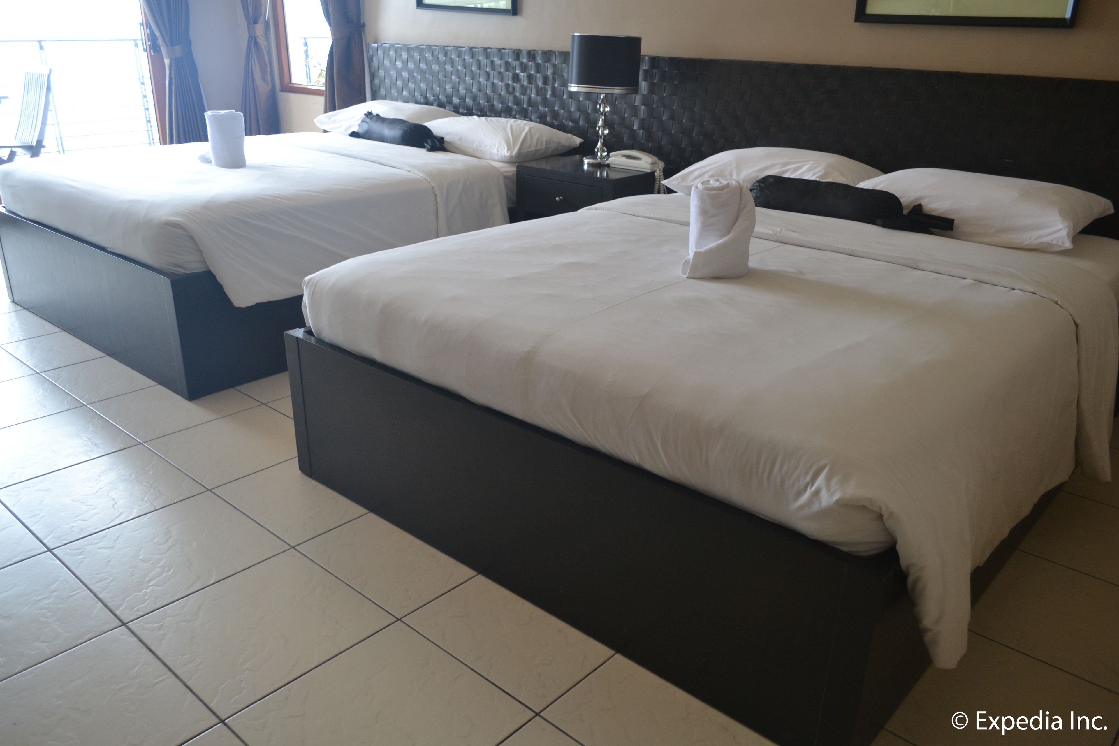 A hotel room with two beds, a nightstand, a lamp, and a framed picture on the wall.