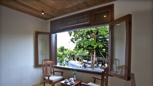 A room with a large window, two wooden chairs, a small table, and a vase with flowers. - Hoi An TNT Villa (Da Nang)