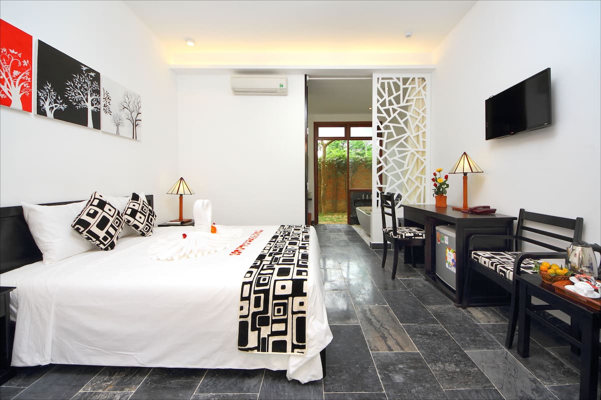 A modern hotel room with a large bed, a desk, a chair, a TV, and artwork on the walls.