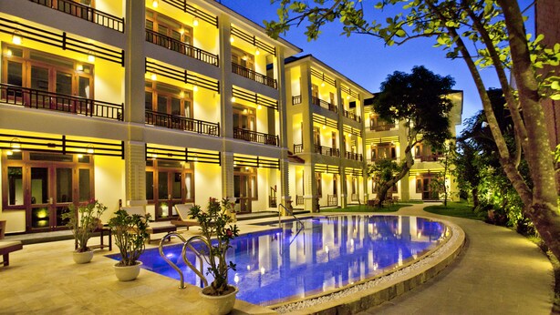 A multi-story hotel with a swimming pool, outdoor seating, and a well-lit facade. - Hoi An TNT Villa (Da Nang)