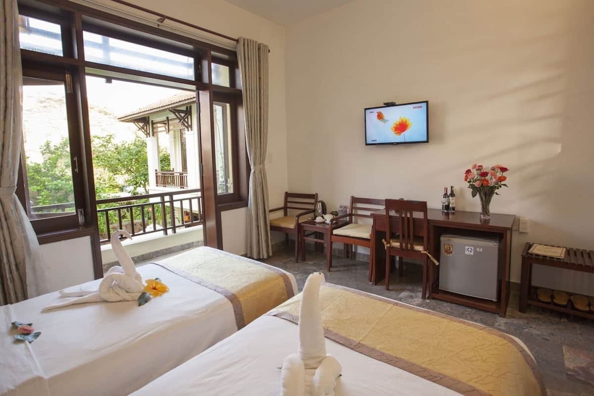A hotel room with two beds, a desk, a chair, a small refrigerator, and a TV on the wall.