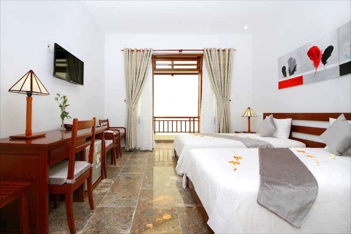 A hotel room with two beds, a desk, chairs, a TV, and a window with curtains.