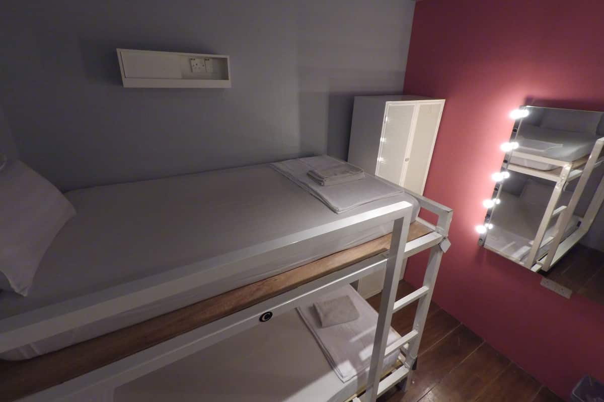 A single-bed room with a wooden headboard, a bedside table, a mirror with lights, and a wardrobe.