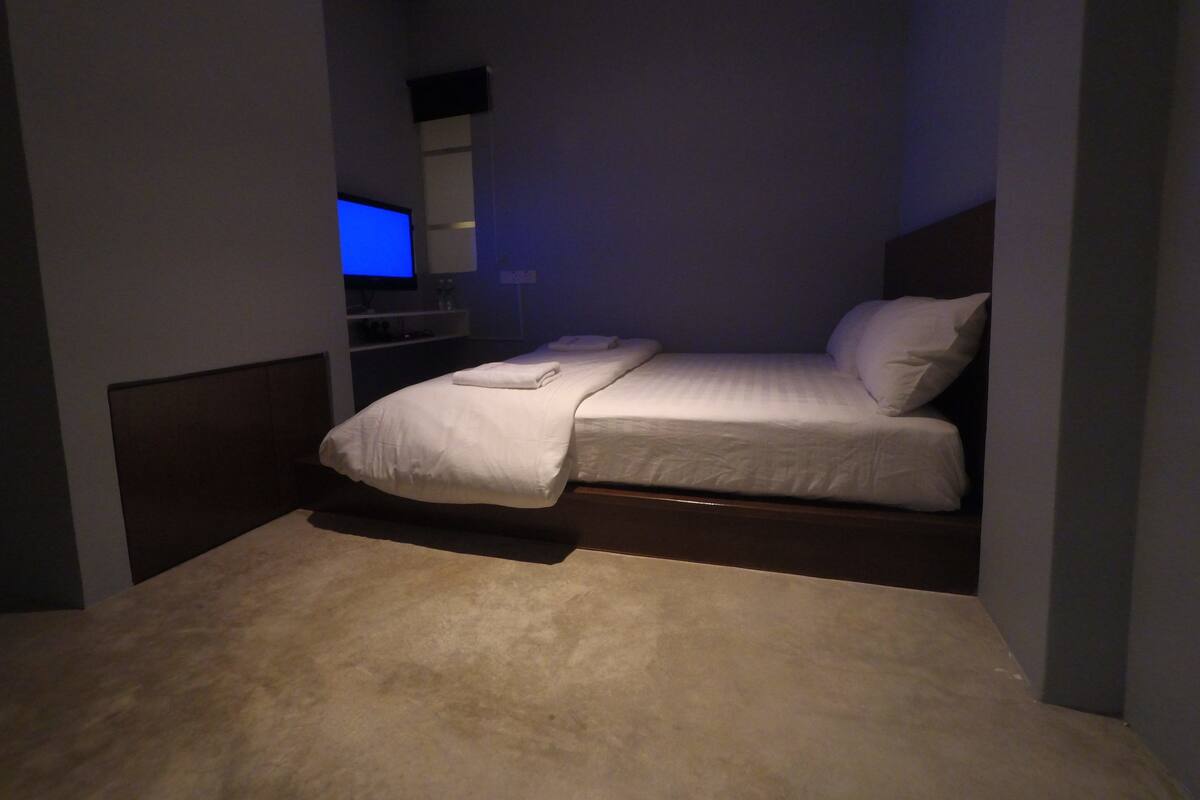 A bedroom with a bed, a TV, and a small shelf with toiletries.