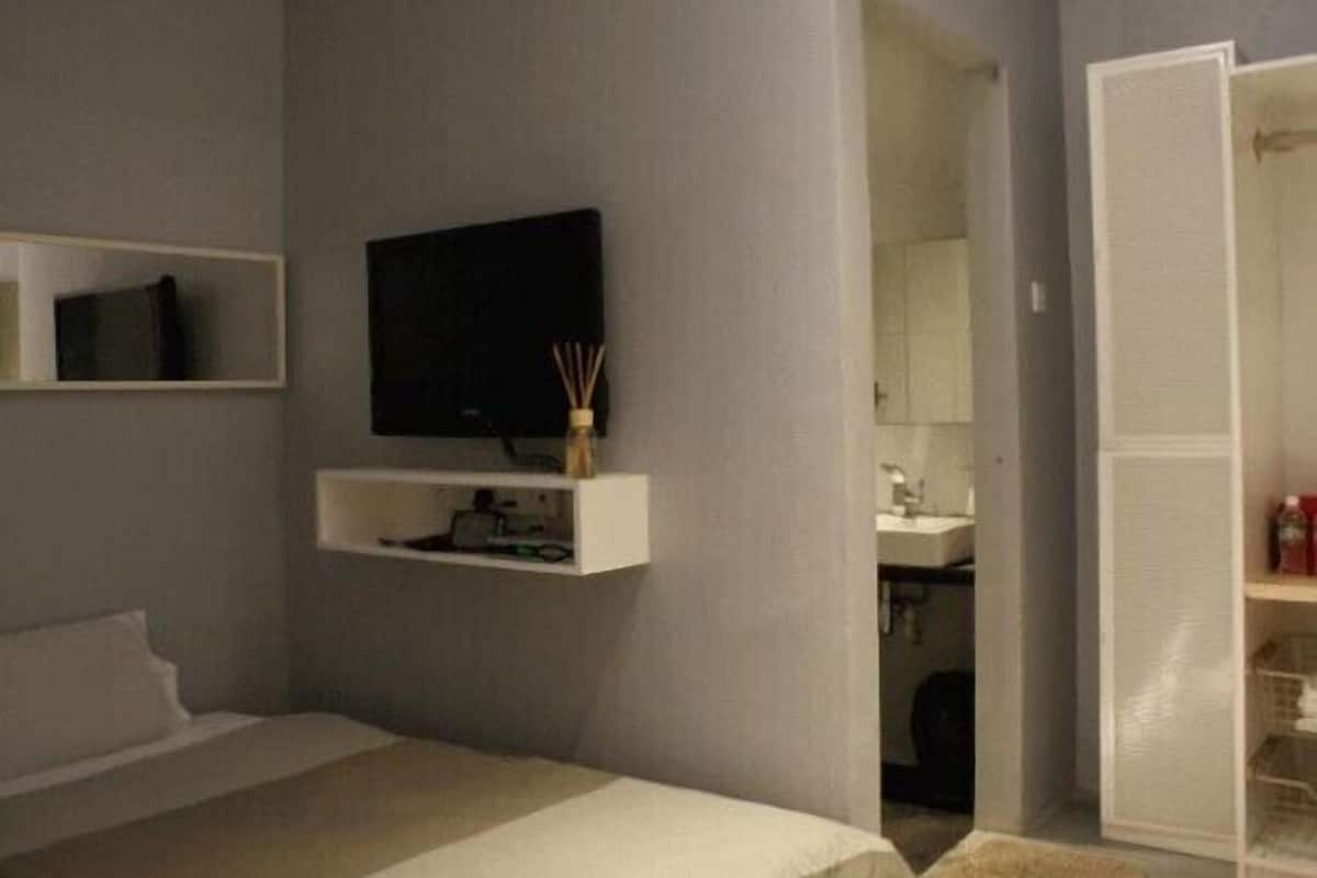 A bedroom with a bed, a TV mounted on the wall, a small shelf with items, and a closet.