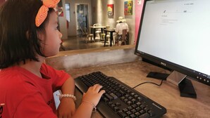 Et barn bruger et tastatur og en Dell-skærm på en café.