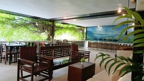 An indoor seating area with wooden furniture, a large mural, and a view of greenery outside. - Travelbee Heritage Inn (Dapitan)