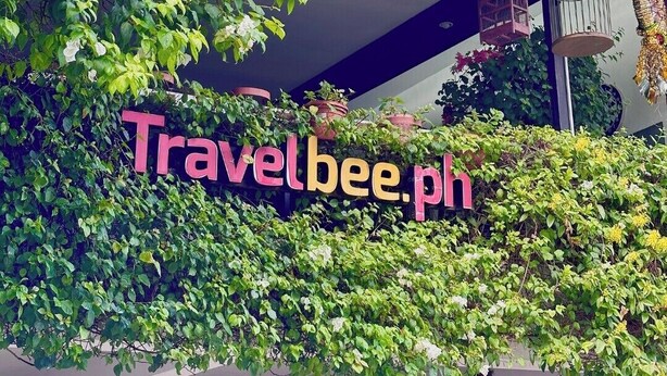 Een Travelbee.ph bord met een weelderige groene klimopachtergrond.