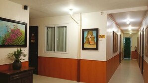 Een hotelgang met een houten vloer, een potplant en kunstwerken in lijsten aan de muren.