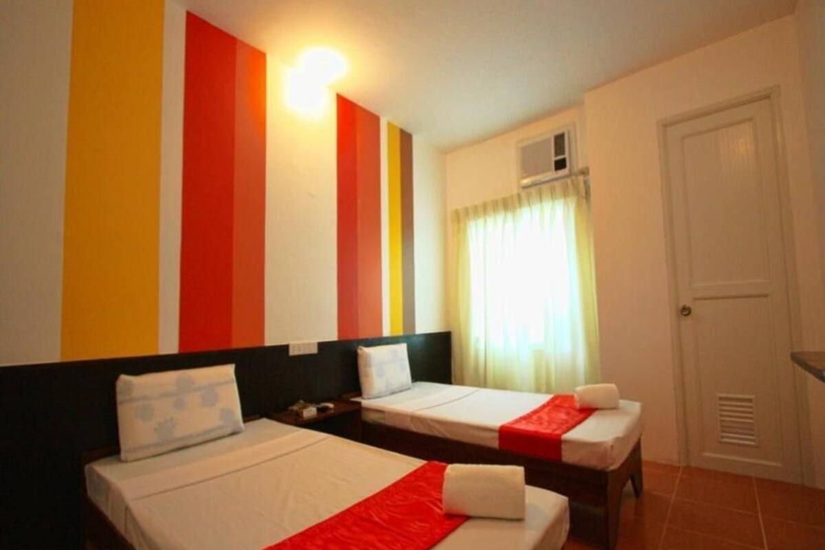 A hotel room with two beds, a window with curtains, a door, and a wall with vertical stripes.