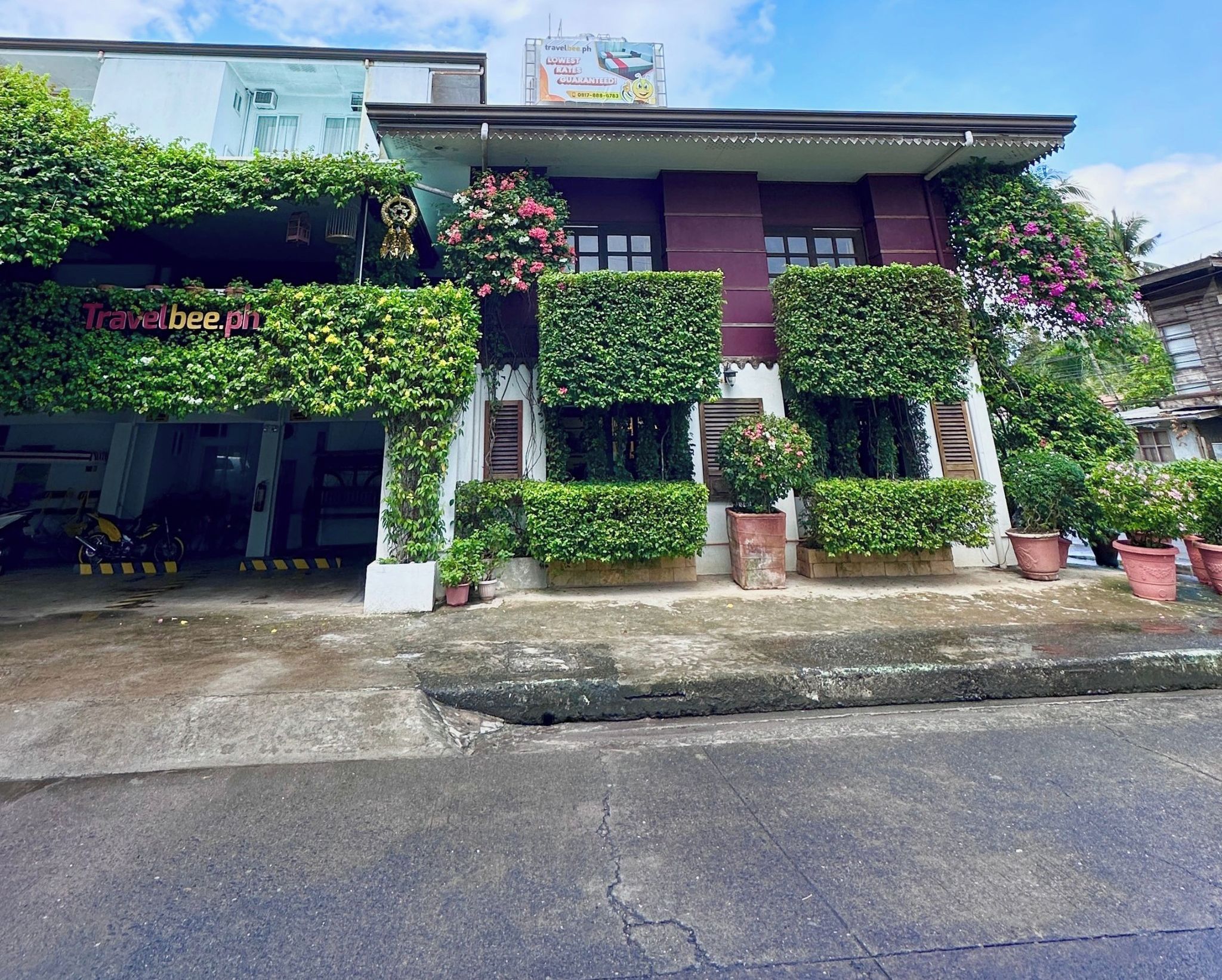 Um edifício com uma placa indicando Travelbee Heritage Inn em Dapitan, apresentando um estilo arquitetônico tradicional com vegetação e flores.