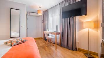 A hotel room with a bed, a desk, a chair, a TV, and a lamp.